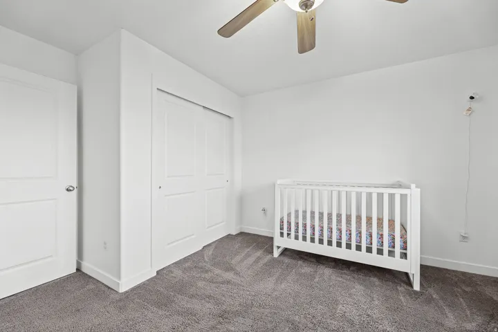 White walls, gray carpet flooring, and a ceiling fan with wood-tone blades