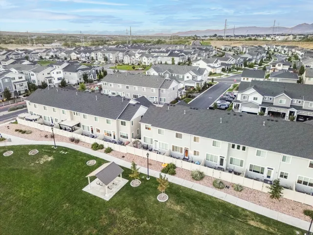 Community with townhomes and detached residences, featuring a shared green space, paved pathways, and covered outdoor seating