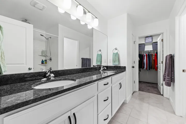Double vanity with undermount sinks, dark stone countertop, white cabinetry, and polished chrome fixtures