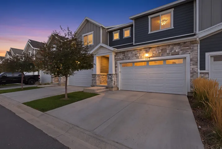 Stone façade detailing, horizontal siding, attached garage, concrete driveway, and established landscaping