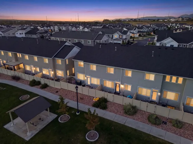 Townhome exteriors with dark roofing, individual fenced patios, and a community green space with a covered picnic area