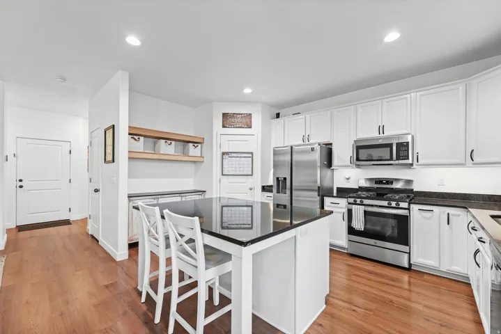 Hardwood-finish flooring, white cabinetry, stainless steel appliances, dark countertops, and a kitchen island with seating