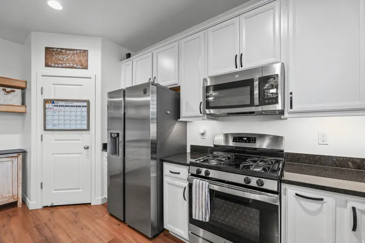 White cabinetry with black hardware, stainless steel appliances, dark stone countertops, wood-finish flooring, and recessed lighting