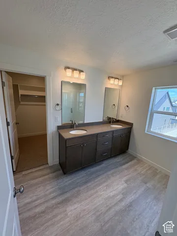 Double vanity with dual sinks, warm-toned wood-finish cabinetry, neutral countertop, and wood-finish flooring
