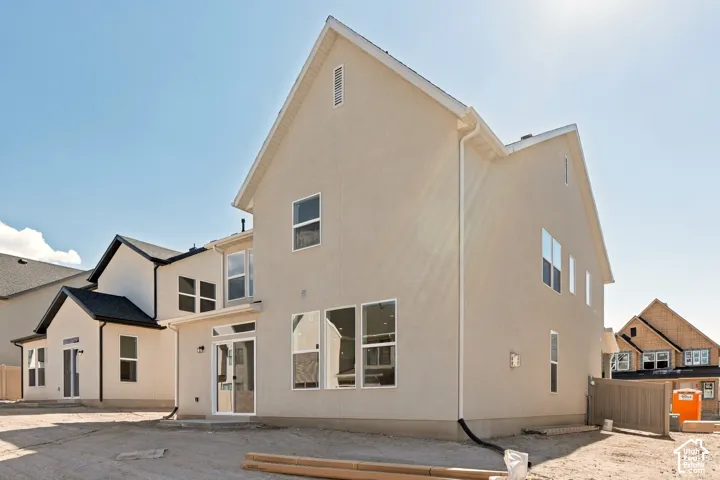 Two-story exterior featuring light-toned stucco siding, a steeply pitched roofline, large multi-pane windows, and a glass sliding door