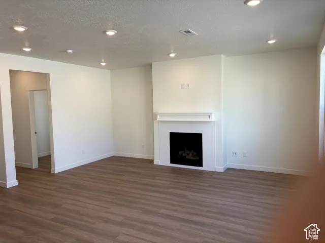 Spacious room featuring wood-finish flooring, recessed lighting, a fireplace with a white mantel, and neutral wall finishes