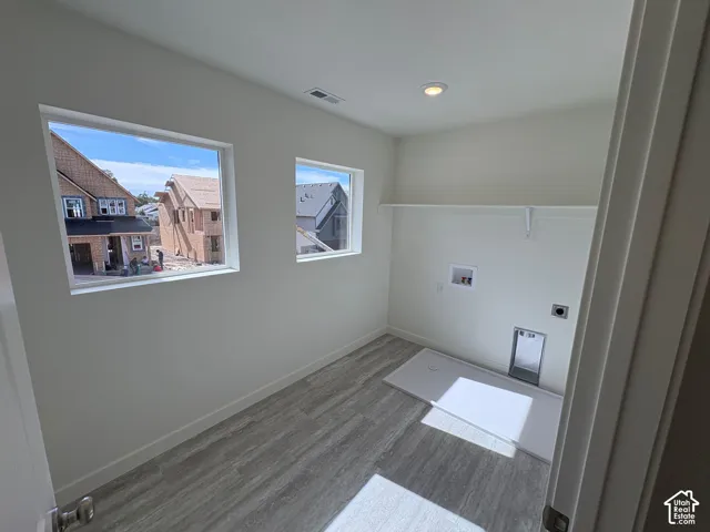 Utility space featuring two windows, wood-finish flooring, a wall-mounted shelf, and laundry connections