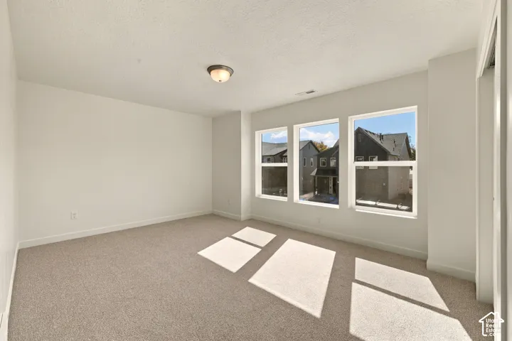Neutral-toned wall-to-wall carpeting, three oversized windows, and a flush-mount light fixture