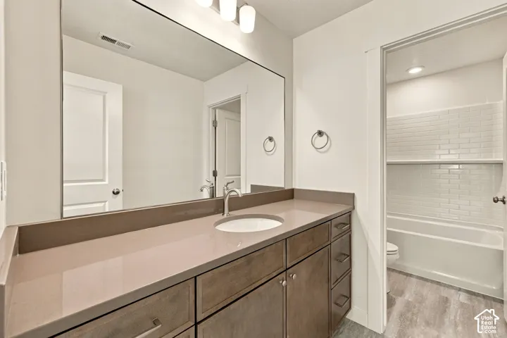 Bathroom featuring a vanity with an integrated basin, smooth-finish countertop, full-width mirror, multi-bulb vanity lighting, and a tub-shower enclosure with subway tile surround