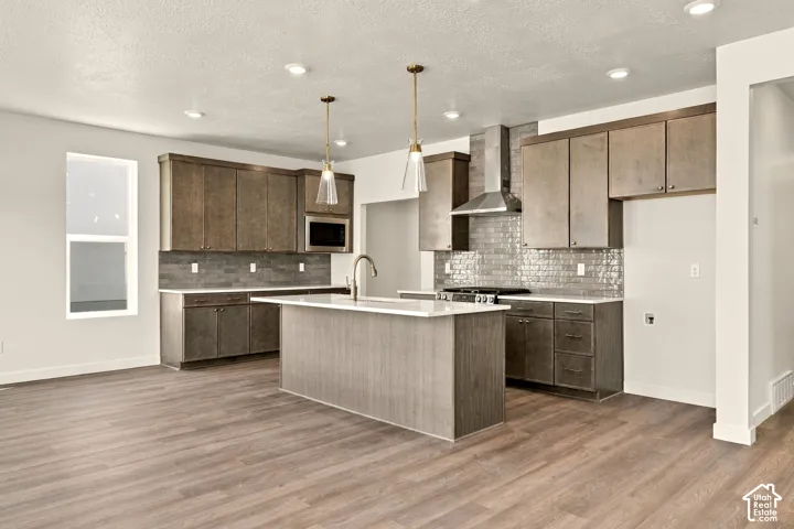 Kitchen featuring flat-panel cabinetry, quartz countertops, subway tile backsplash, stainless steel range hood, and wood-finish flooring