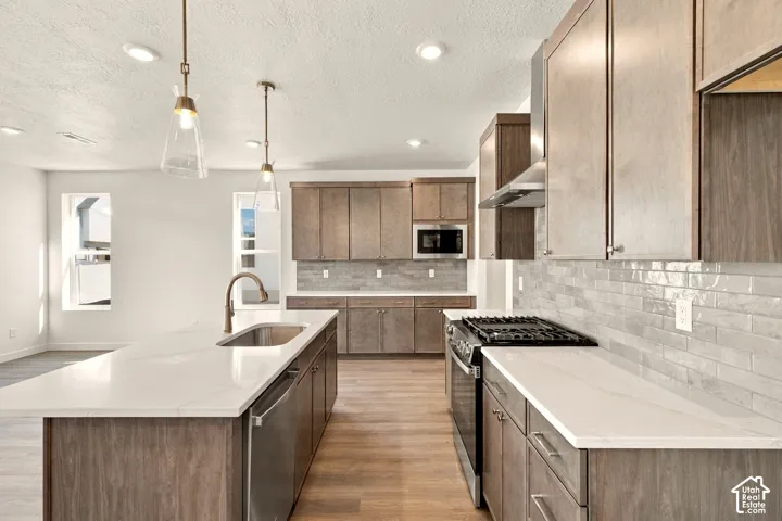 Kitchen featuring wood-finish cabinetry, stone-surface countertops, subway tile backsplash, stainless steel appliances, and a central island with an undermount sink