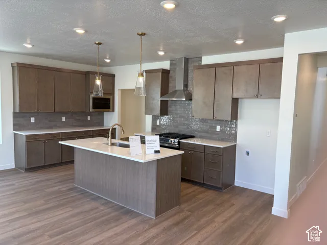 Kitchen featuring an island with a built-in sink, wood-finish flooring, recessed lighting, and pendant lights