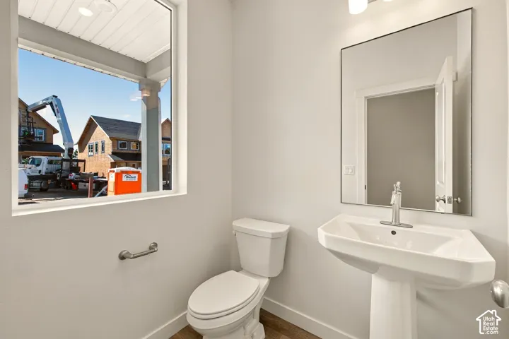 Pedestal sink with single-handle chrome faucet, rectangular wall mirror, wood-finish flooring, and wall-mounted grab bar