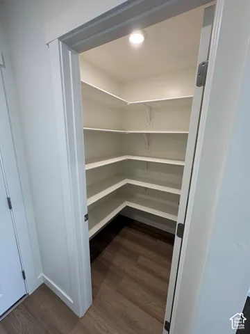 Walk-in pantry featuring white shelving, wood-finish flooring, and recessed lighting