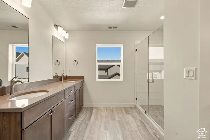 Dual-sink vanity with a solid-surface countertop, wood-finish cabinetry, wood-finish flooring, and a glass-enclosed walk-in shower