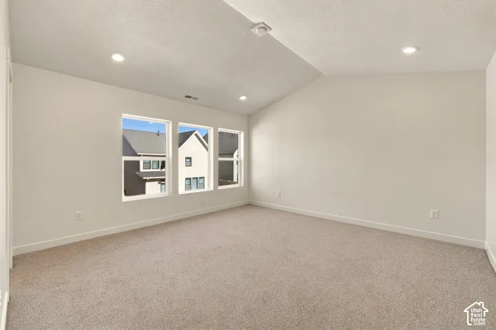 Interior space featuring a vaulted ceiling, neutral wall tones, wall-to-wall carpeting, and recessed lighting, accented by three large windows