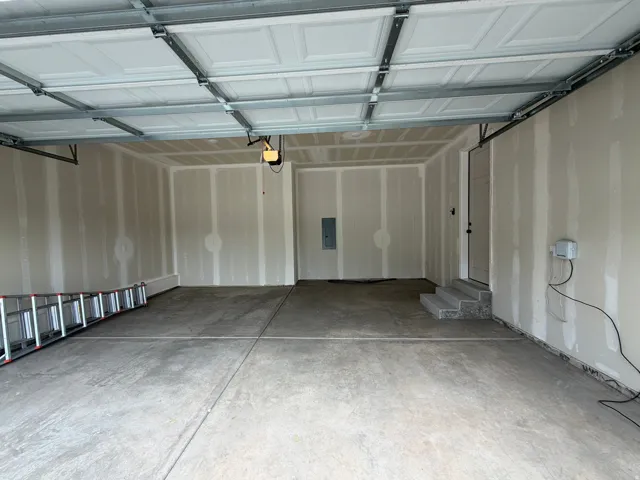 Spacious garage with exposed drywall, concrete flooring, and a panel-style garage door