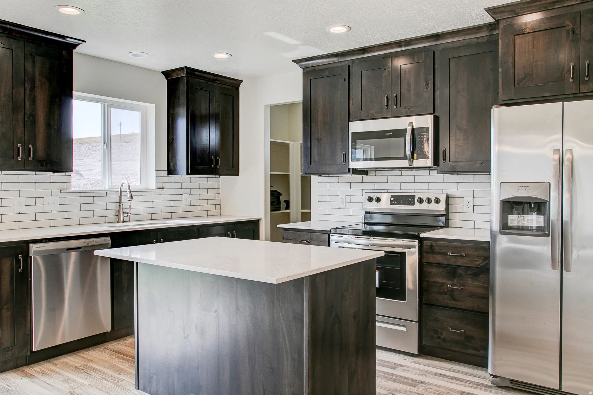 Kitchen featuring dark wood-finish cabinetry, stainless steel appliances, a center island with a white countertop, and a white subway tile backsplash