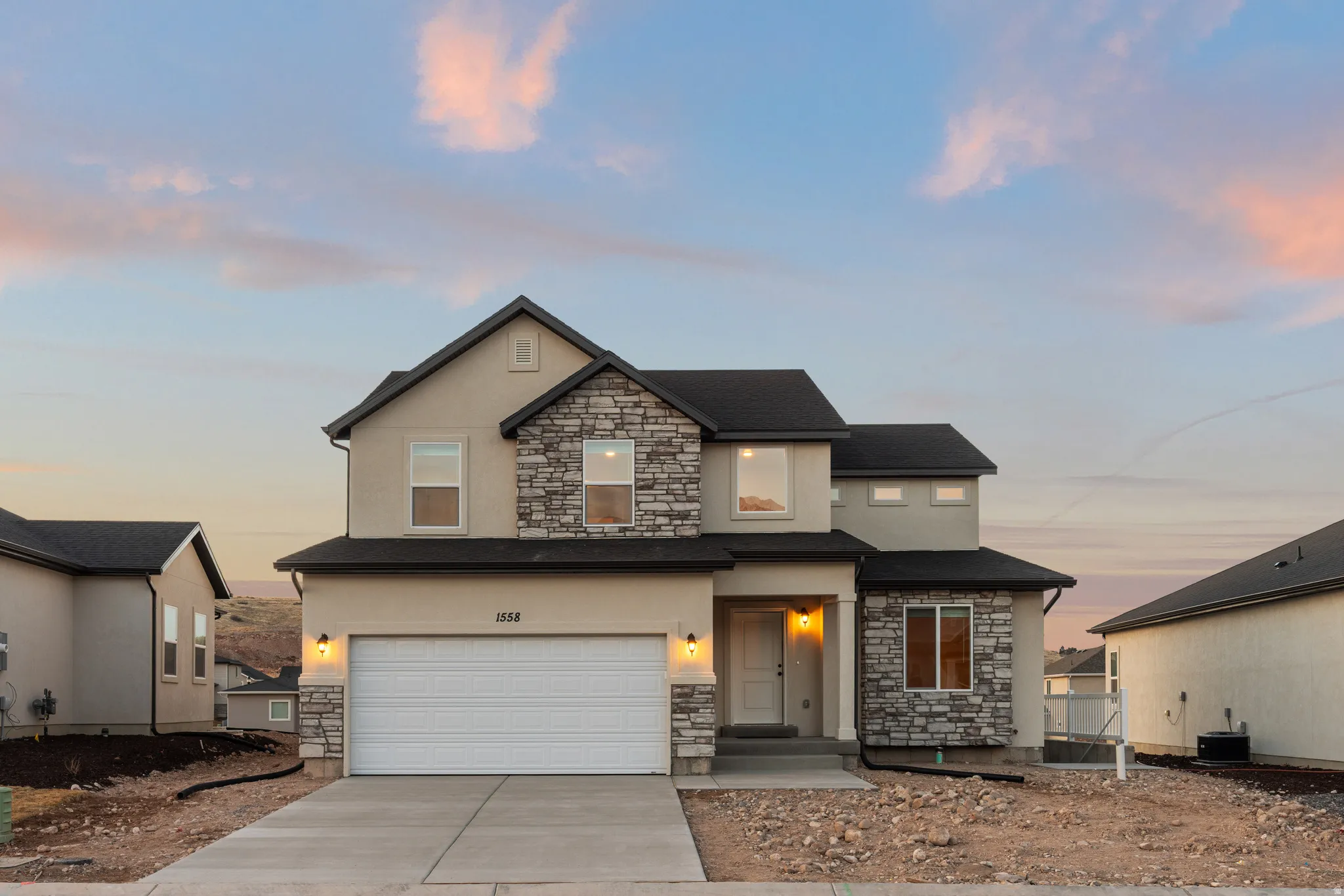 Two-story stucco exterior with stone accents, attached garage, concrete driveway, and front entryway