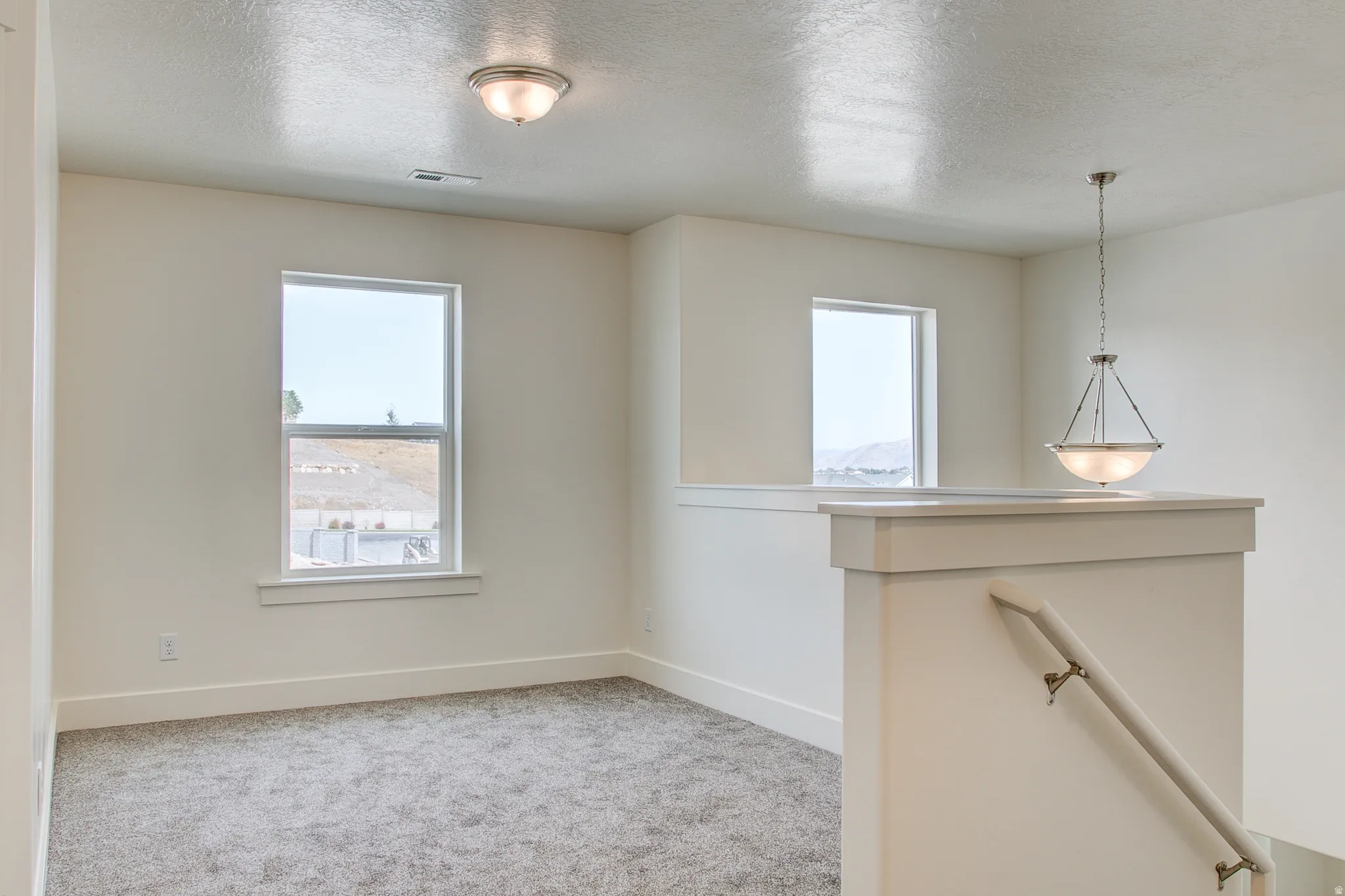 Plush carpeting, neutral wall tones, two pane windows, a flush-mount ceiling light, and a hanging pendant light