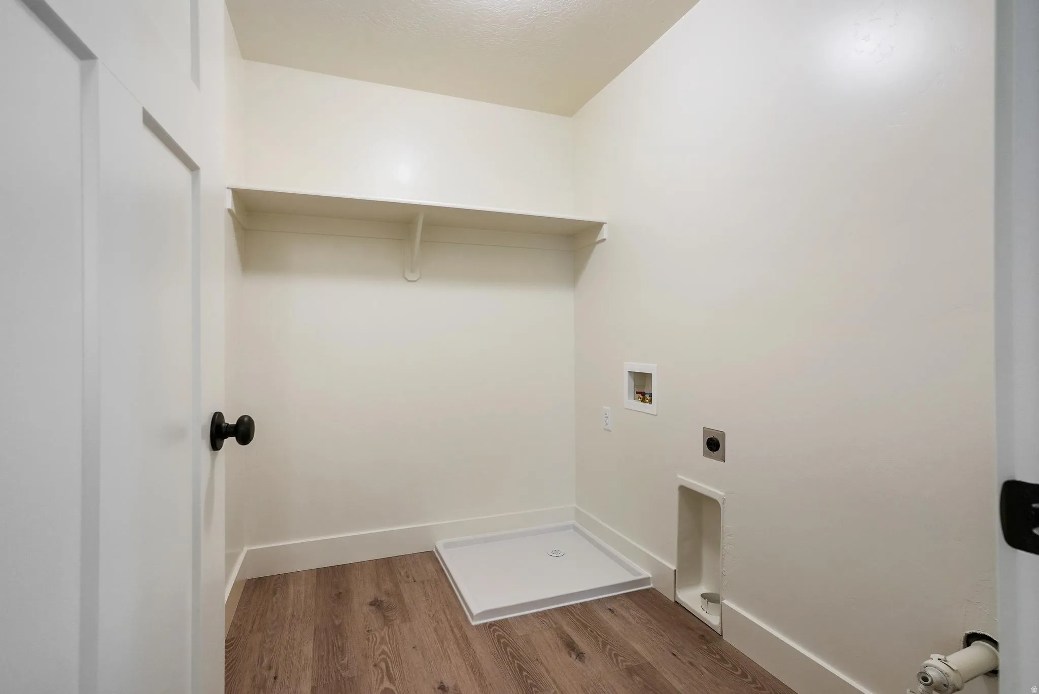 Wood-finish flooring with white baseboards, utility hookups, and a wall-mounted shelf