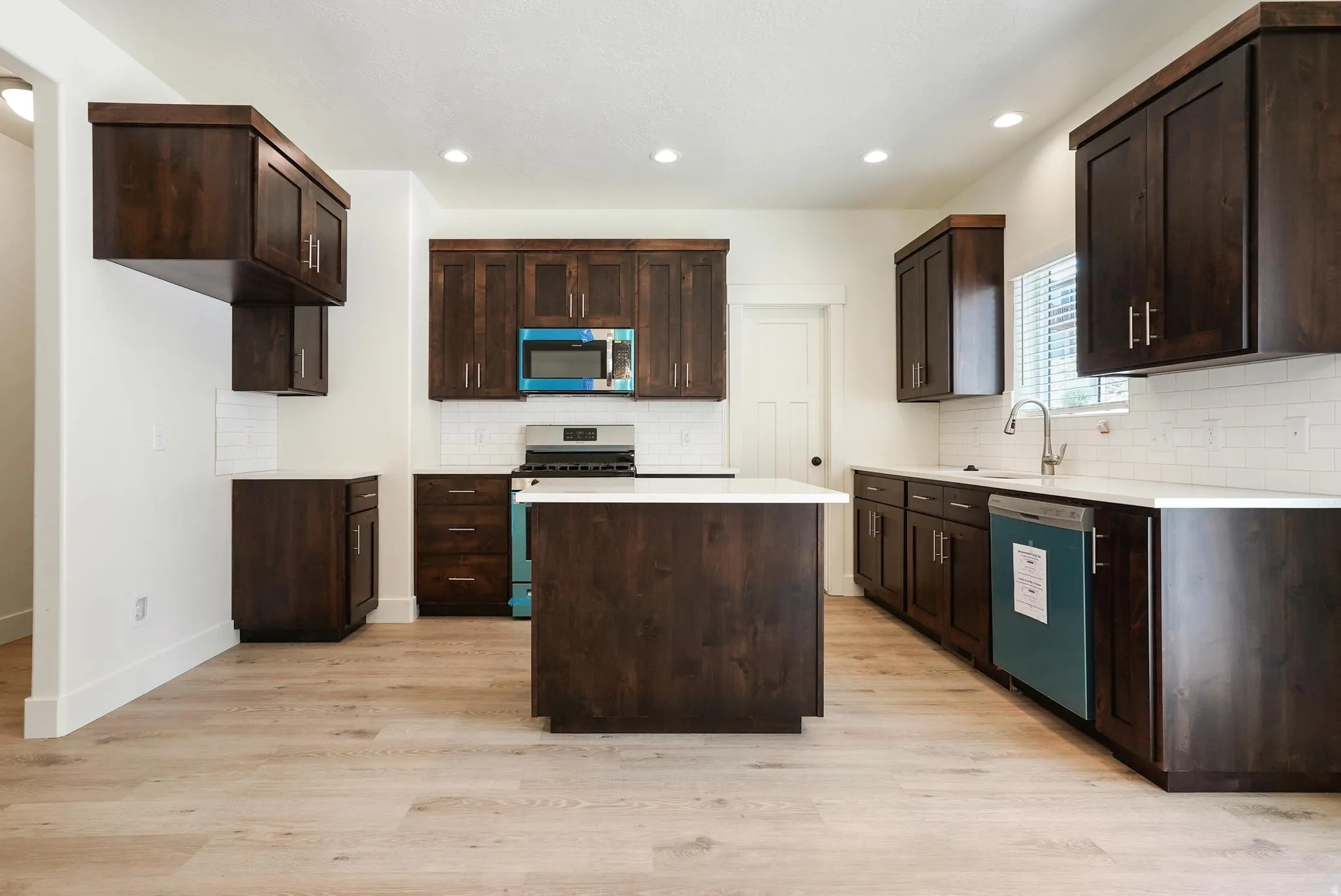 Expansive kitchen featuring dark wood cabinetry, light-toned wood-finish flooring, white countertops, and a subway tile backsplash