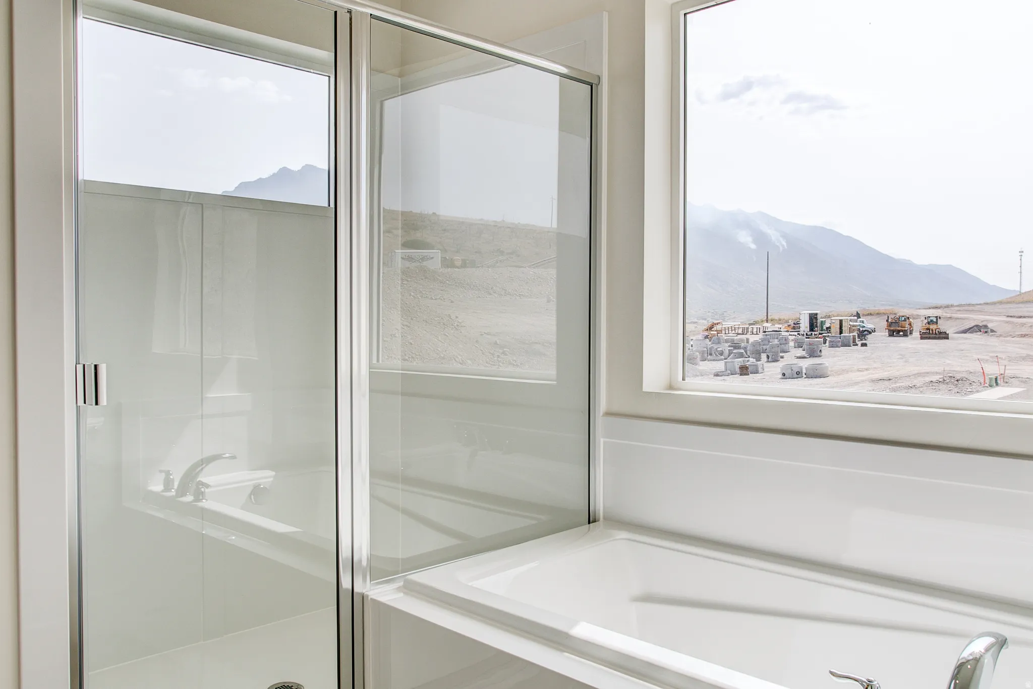 White built-in bathtub with a polished chrome faucet, glass-enclosed shower, and a large window