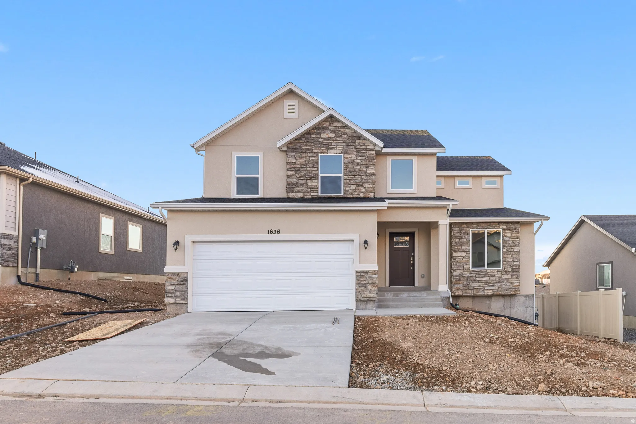 Two-story stucco and stone exterior featuring an attached garage, covered entryway, and concrete driveway