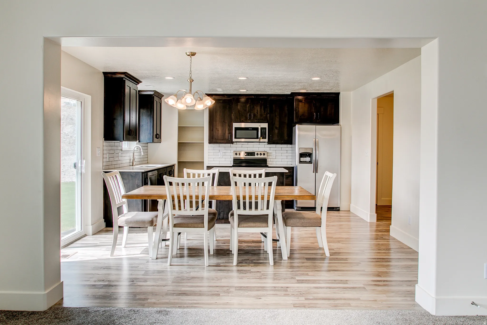 Open-concept dining area featuring wood-finish flooring, a contemporary chandelier, and a sliding glass door