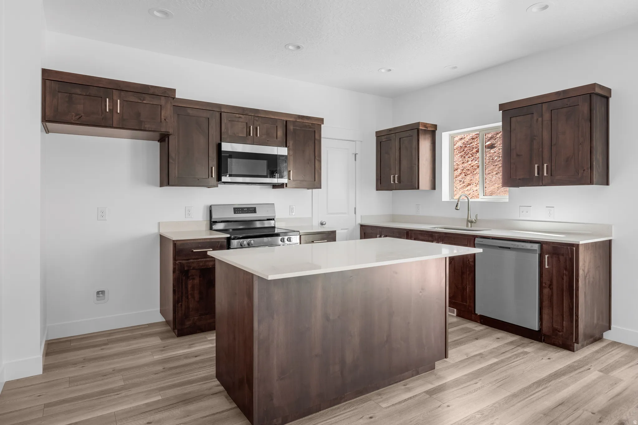 Kitchen featuring wood-finish flooring, dark wood cabinetry, white countertops, stainless steel appliances, and a central island