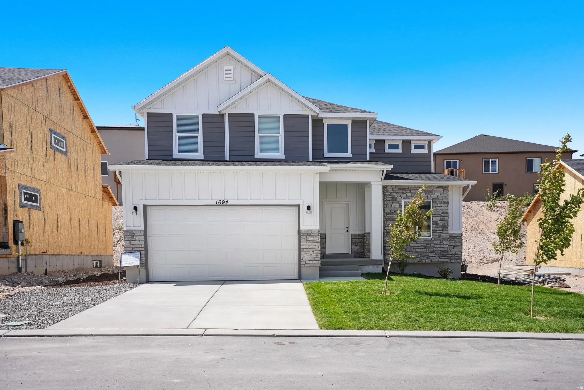 Two-story facade with mixed material siding, stone accents, attached two-car garage, concrete driveway, and a covered entry porch