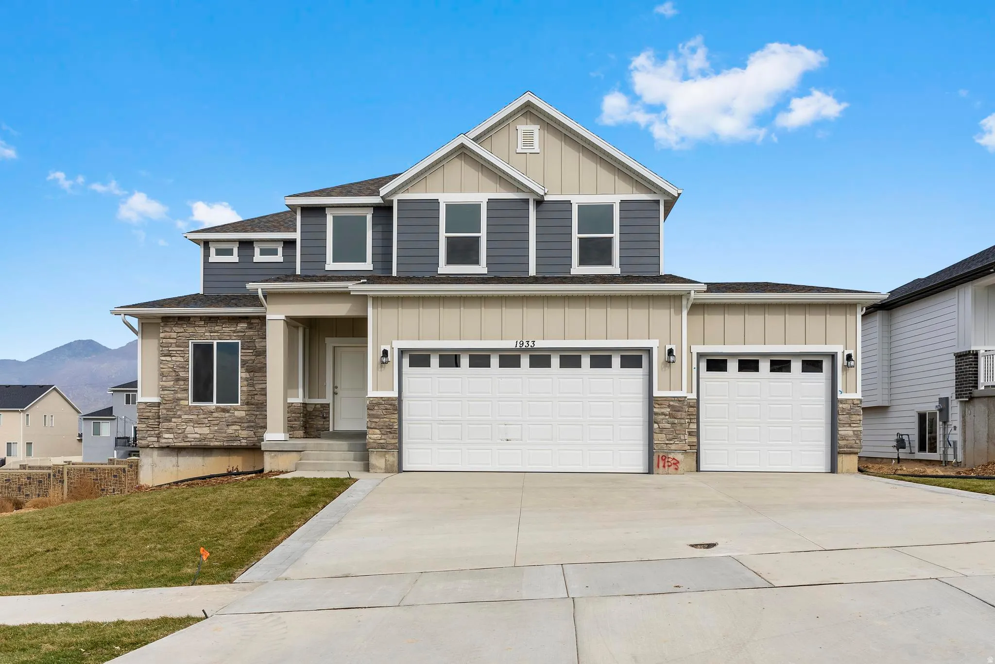 Two-story residence featuring a stone and siding exterior, multi-panel garage doors, a covered entry, and a concrete driveway