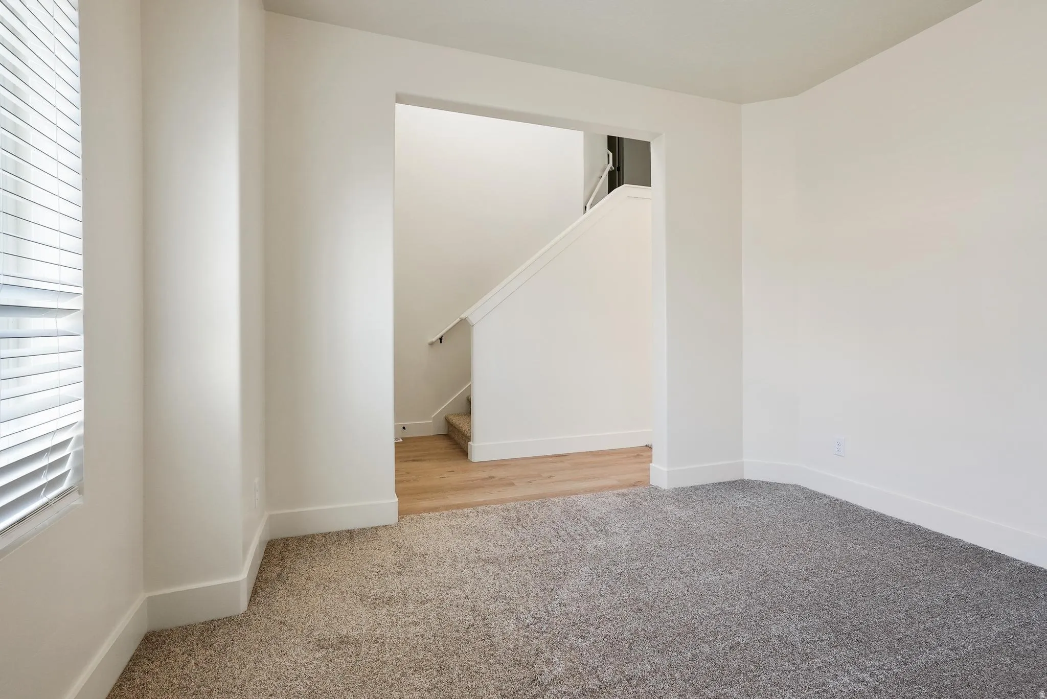 Open entryway featuring light wood-finish flooring, staircase with white risers, and a carpeted room with a window