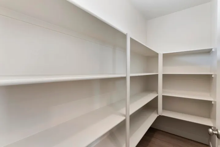 Walk-in pantry featuring extensive white shelving and wood-finish flooring