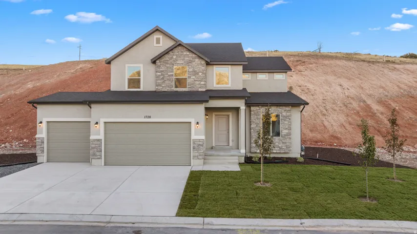 Contemporary facade with stucco and stacked stone accents, dark-shingle roof, two-car garage, and established landscaping