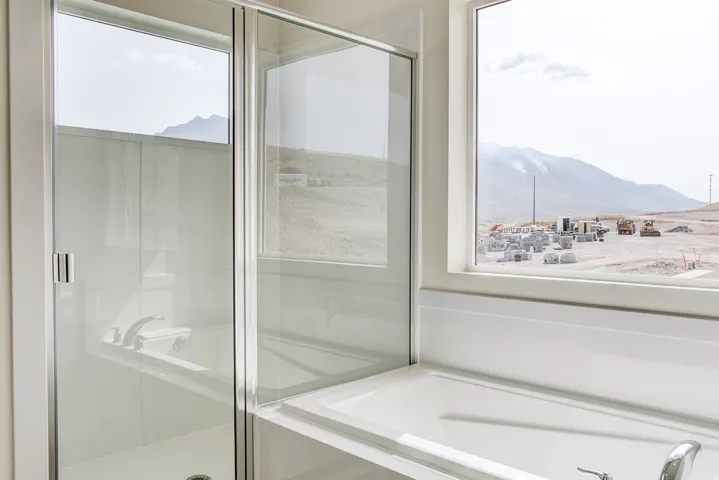 White built-in bathtub with a polished chrome faucet, glass-enclosed shower, and a large window