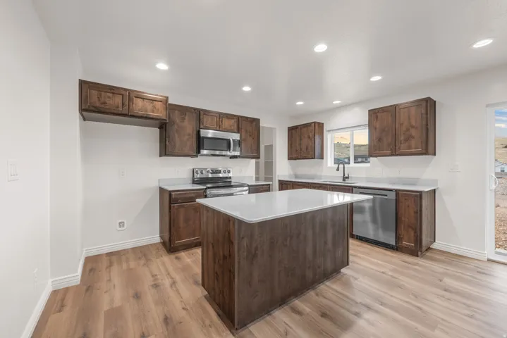 Kitchen featuring rich wood-finish cabinetry, light countertops, a central island, recessed lighting, and stainless steel appliances