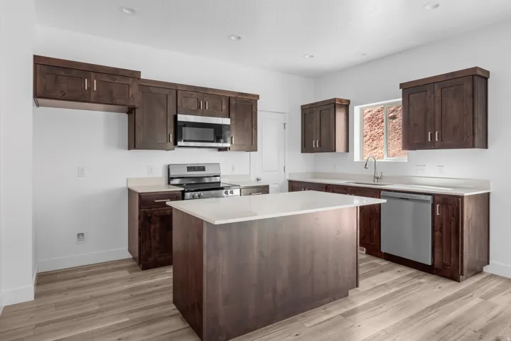 Kitchen featuring wood-finish flooring, dark wood cabinetry, white countertops, stainless steel appliances, and a central island