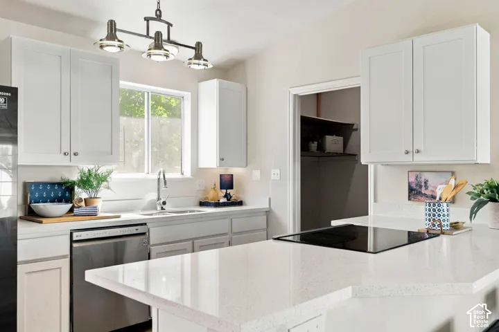 White shaker-style cabinetry, stainless steel dishwasher, integrated cooktop, light-toned countertops, and a built-in pantry