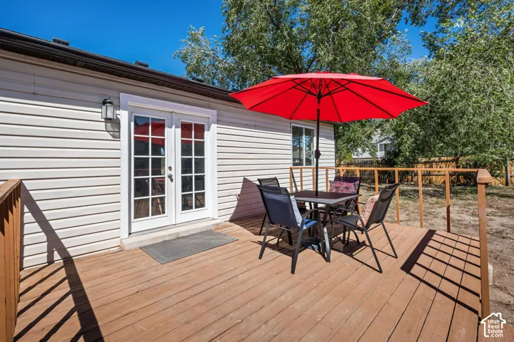 Expansive wooden deck featuring perimeter railing, dual-pane glass French doors, exterior wall sconce, and horizontal siding