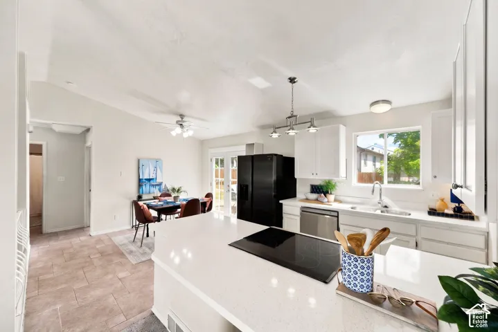 Open-concept kitchen and living area featuring white cabinetry with integrated appliances, a black gas cooktop with island seating, quartz countertops, stainless steel sink, large windows with natural light, wood-finish flooring, and ceiling fans througho