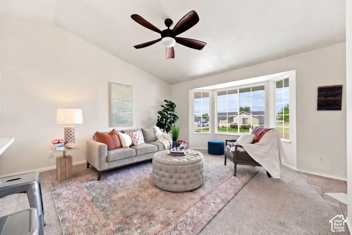 Vaulted ceiling with a ceiling fan, bay window, and carpeting