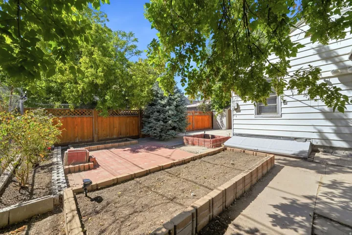 Paved patio space, raised garden beds, wood fencing, and mature trees