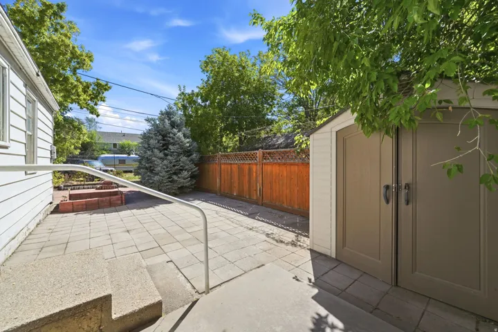 Expansive paver patio with mature shade trees and wooden privacy fencing