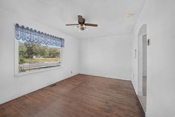 Wood-finish flooring, ceiling fan with light fixture, and a large window with horizontal blinds