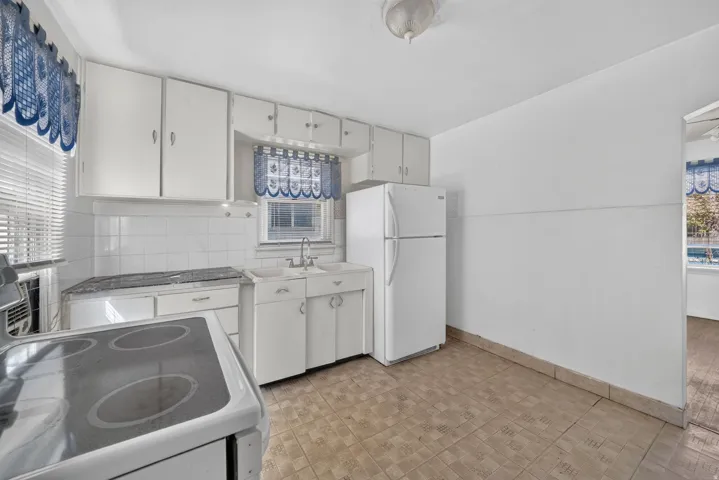 Kitchen featuring white cabinetry, white tile backsplash, a built-in sink, white refrigerator, and tile flooring