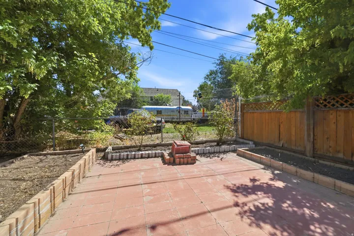 Expansive outdoor patio with terracotta-style pavers, brick-edged planter beds, and wood fencing