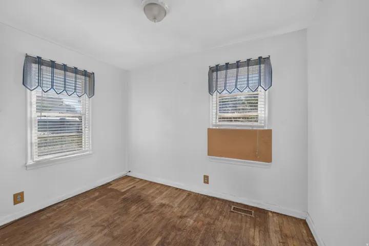 White walls with wood-finish flooring, featuring two windows with blinds