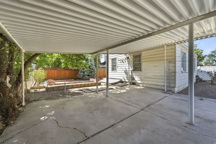 Covered concrete patio with metal support posts, wood fence, and exterior siding