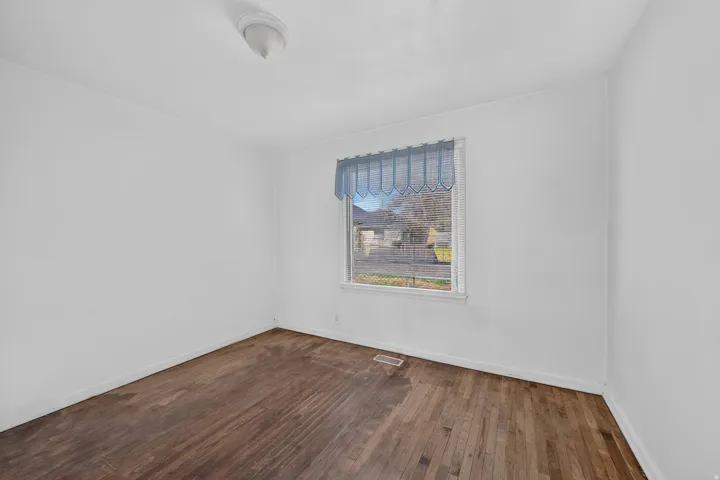 Hardwood flooring, white painted walls, and a single window